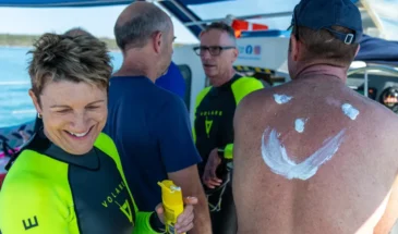 Swimmer laughing while applying sunscreen to another swimmers back in the shape of a smiley face.