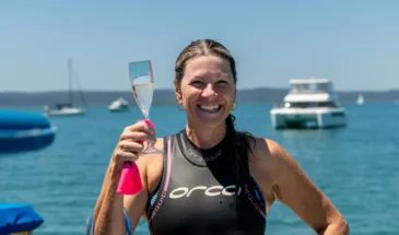 Swimmer smiling and holding a glass of bubbly drink on a yacht at Moreton Bay